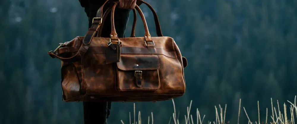 Person holding leather duffel bag in wilderness